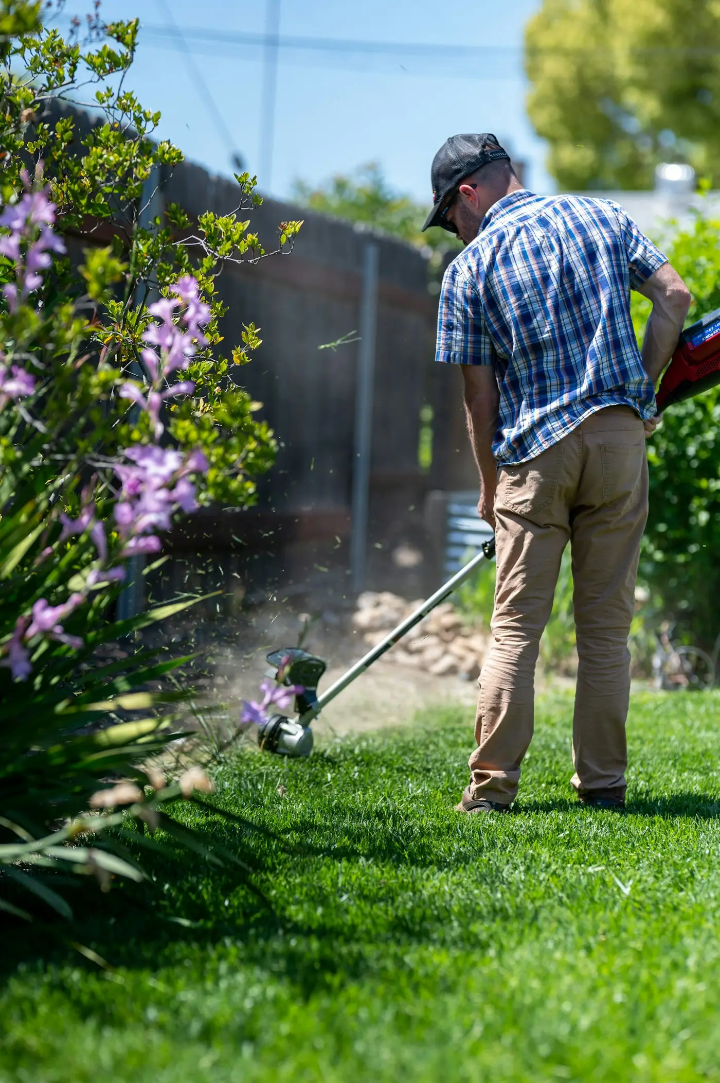 Gardener strimming the lawn edge along a flower border