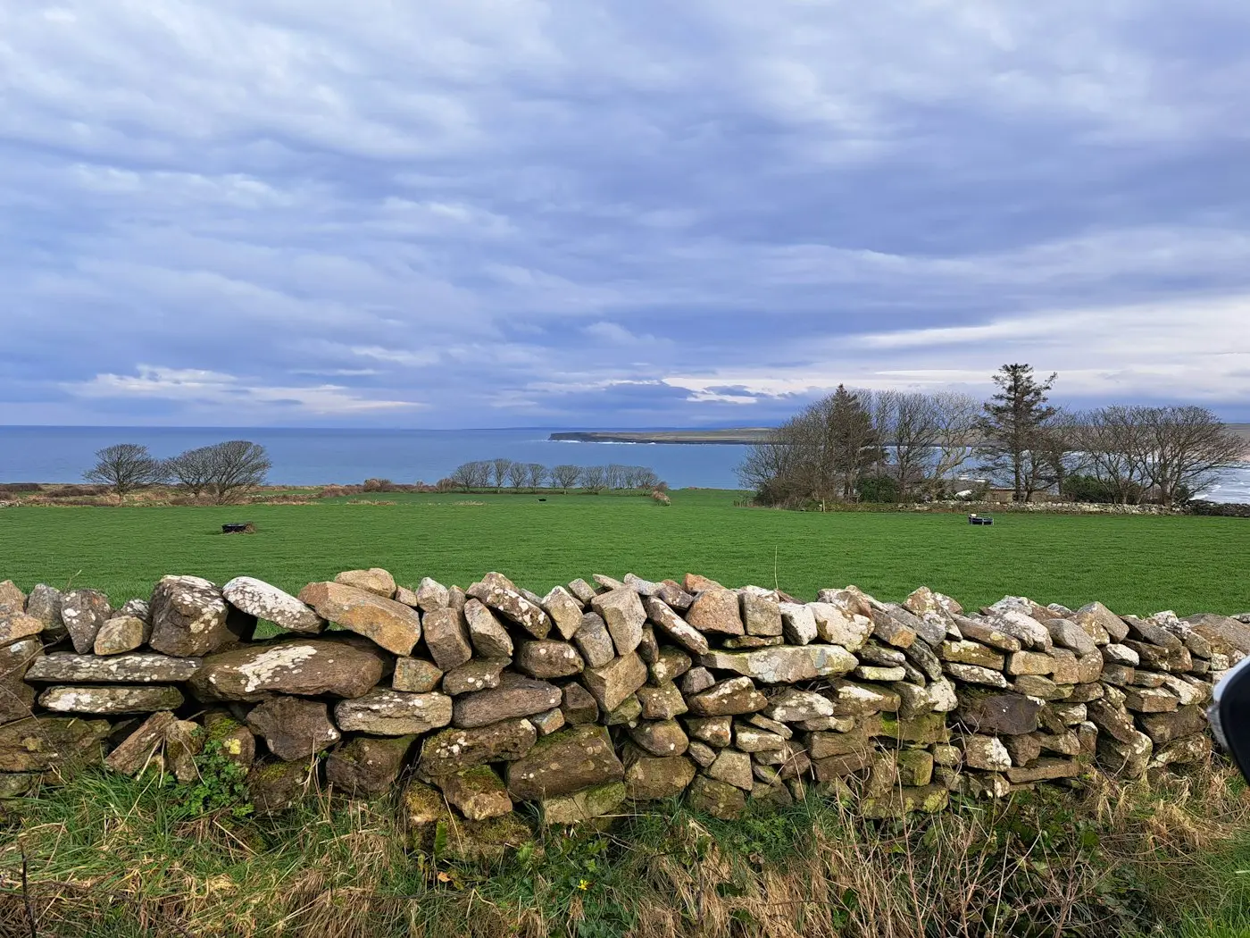 Dry stone wall crossing a green field under a grey sky